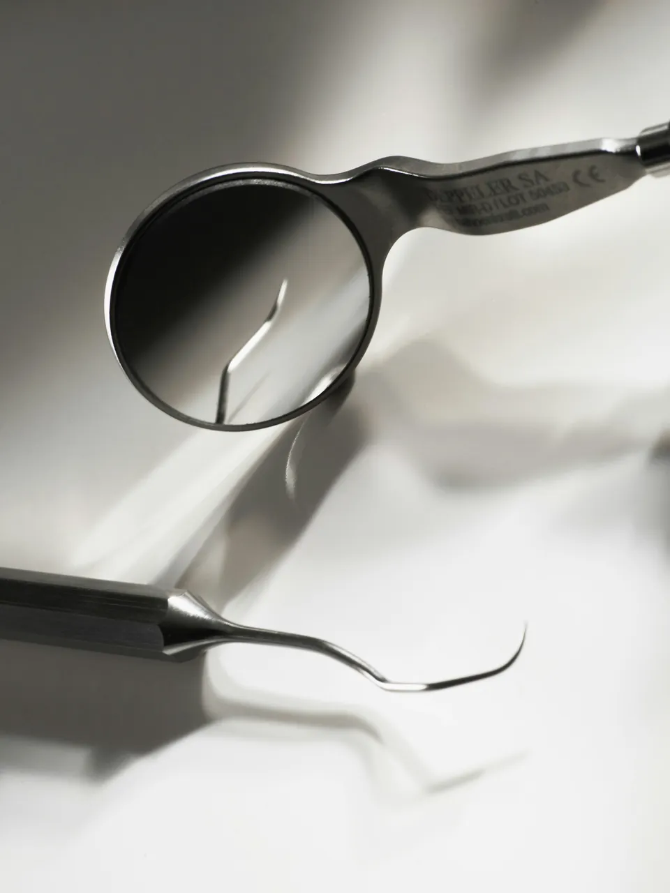 A dental mirror and explorer on a white surface